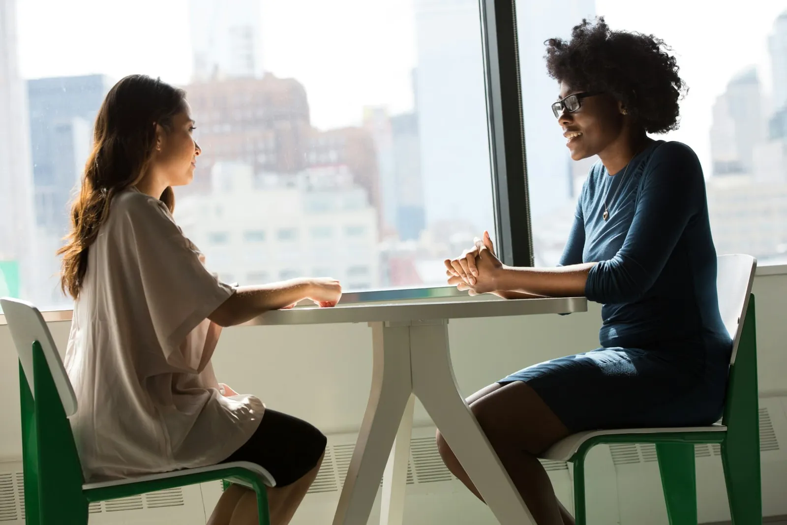 Two women having a supportive conversation beside a large window.