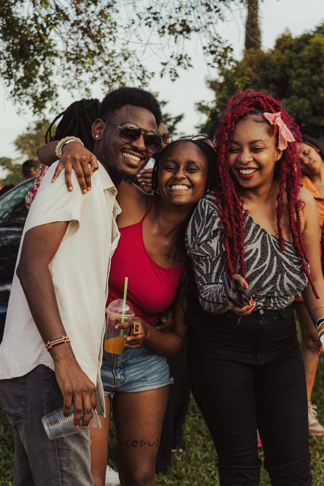 Three Black young adults laughing and embracing outdoors.